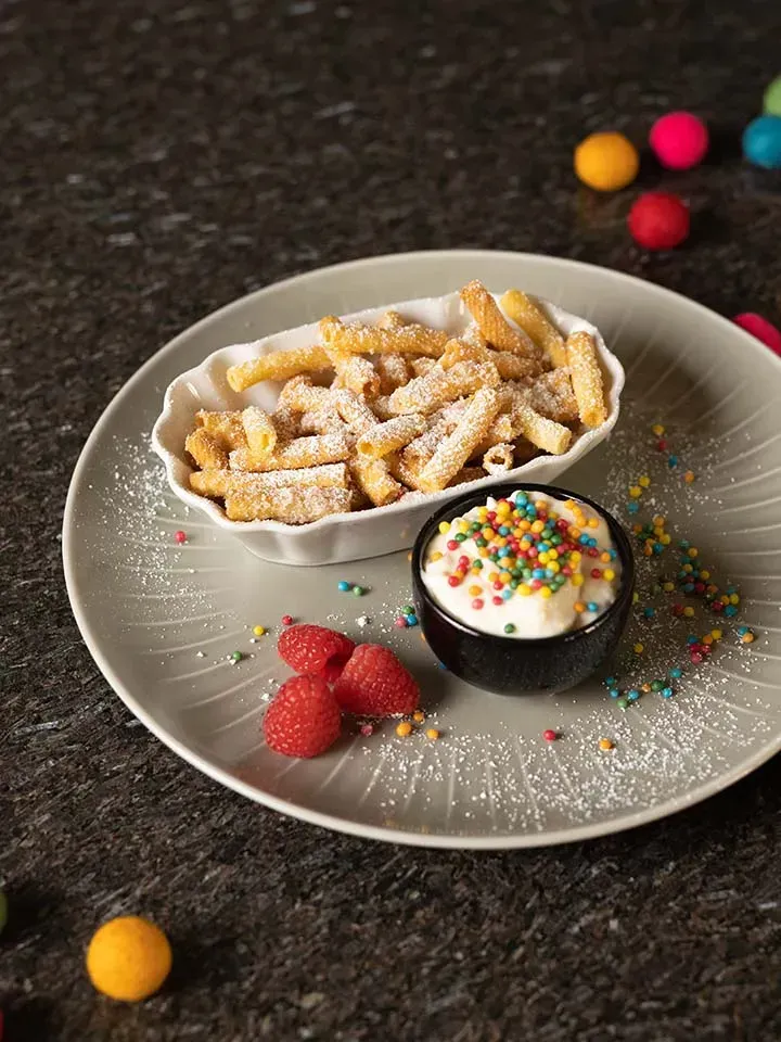 Nudelchips aus Makkaroni mit Staubzucker, Dip mit bunten Streuseln und frische Himbeeren auf einem Teller