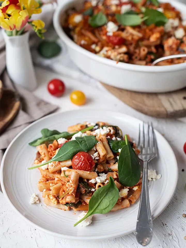 Vegetarisches Nudelgratin mit Spinat und Tomaten auf einem Teller, daneben eine Gabel