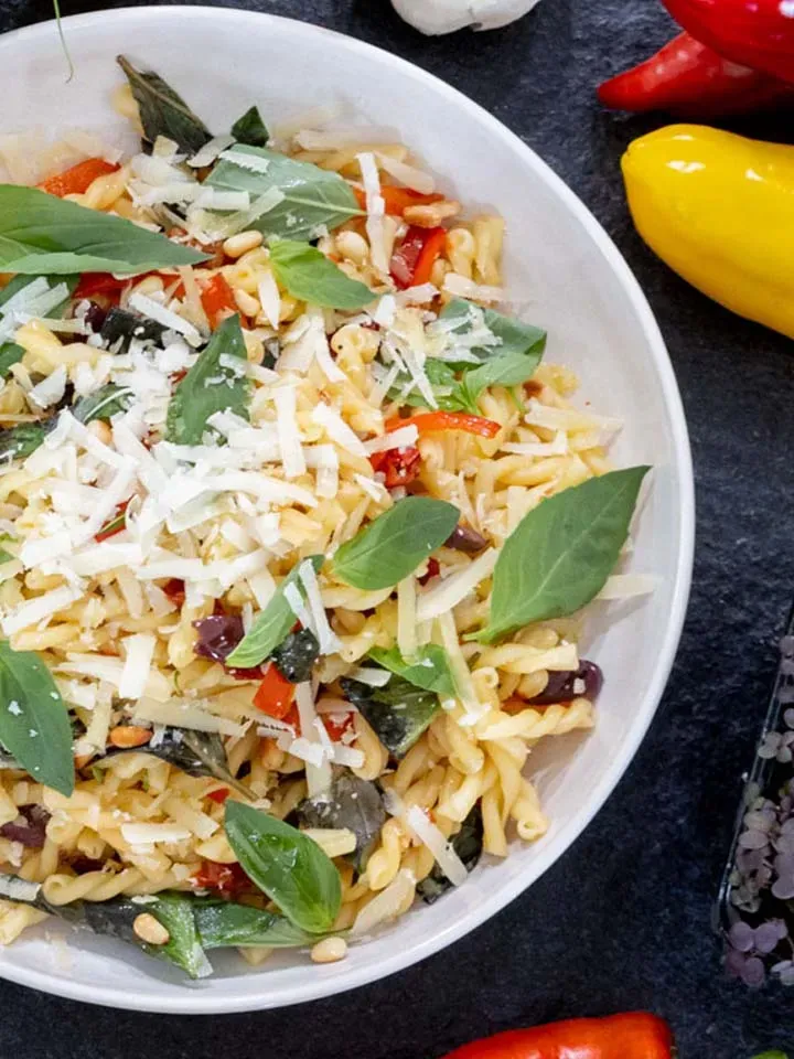 Nudeln Arrabbiata mit Basilikum, geriebenem Käse und Gemüse in einer Schüssel auf dunklem Untergrund