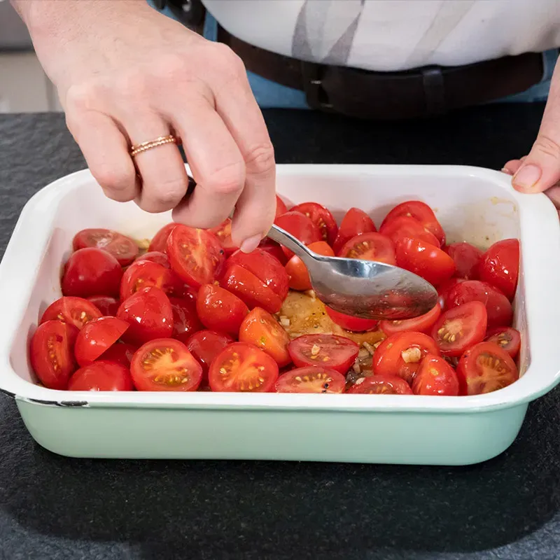 Hand verteilt mit einem Löffel Tomatenhälften in einer Auflaufform für Nudeln Caprese