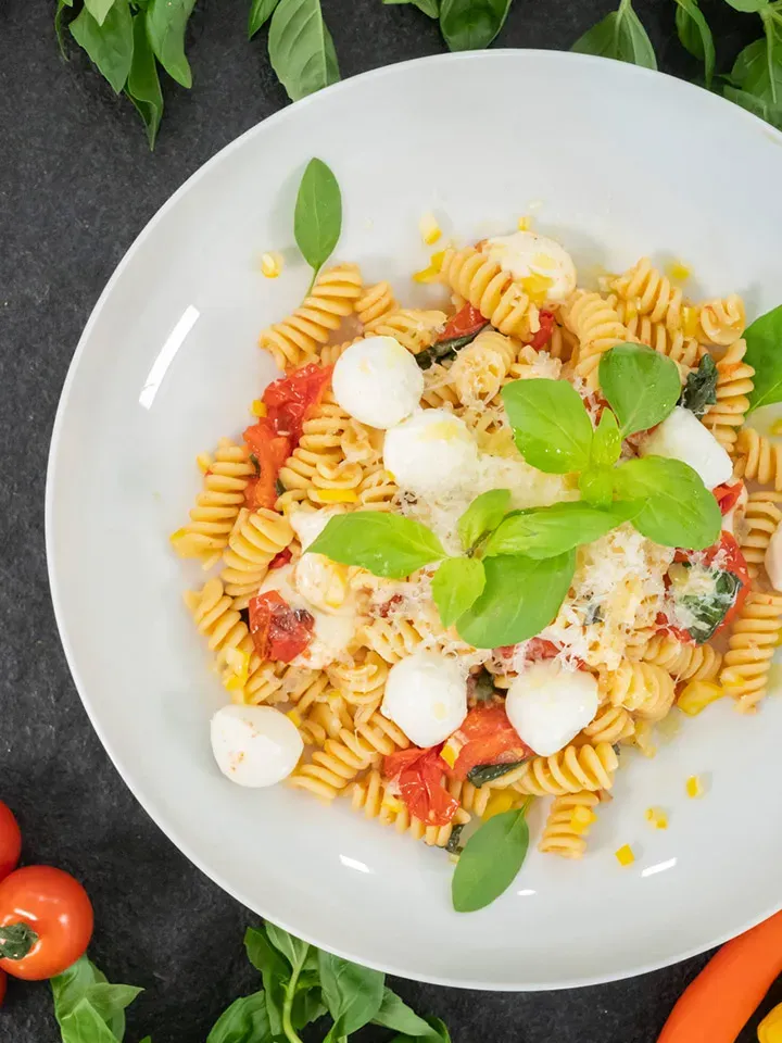 Nudeln Caprese mit Paradeiser und Mozzarella: Fusilli mit Tomaten und Basilikumblättern auf einem Teller