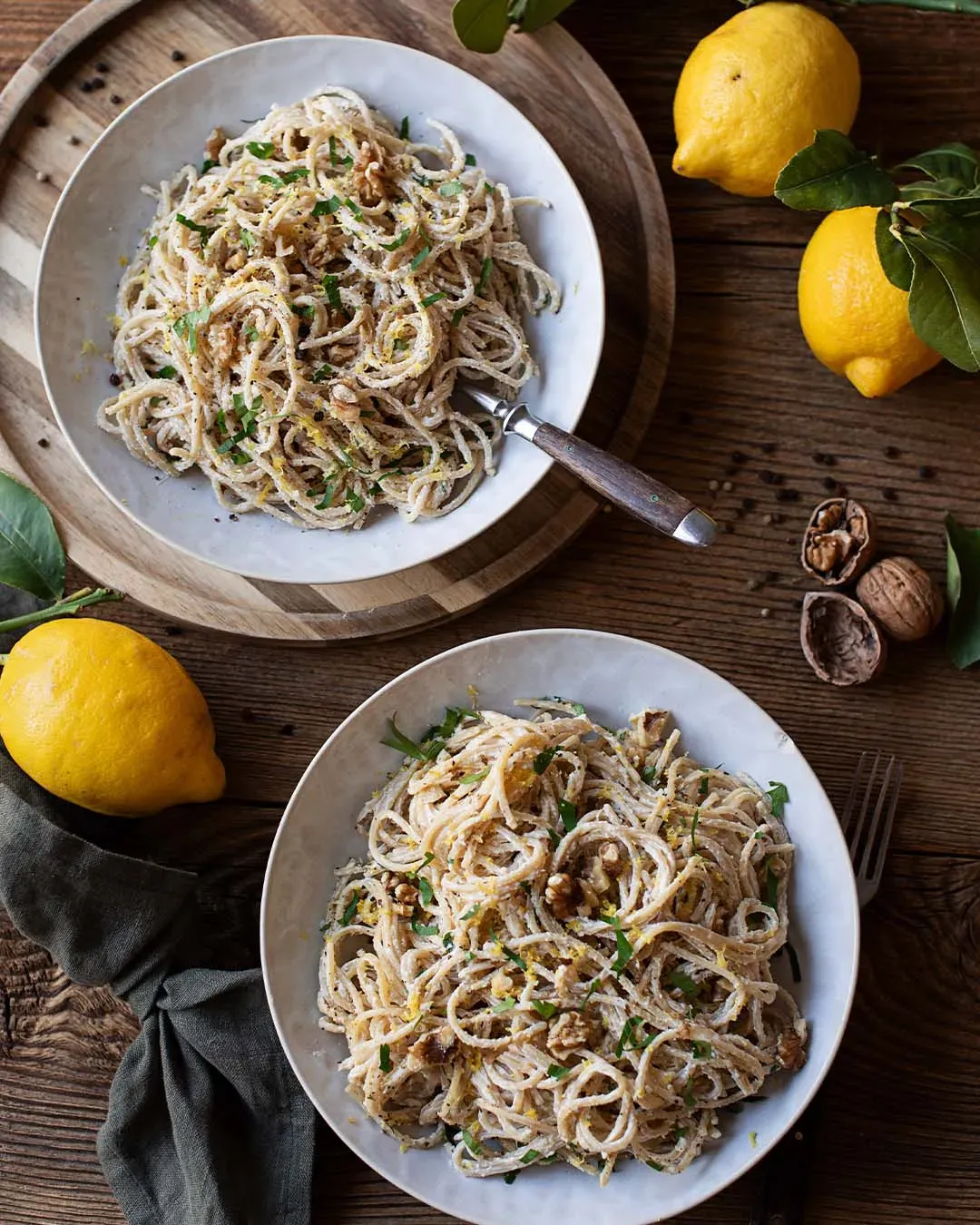Nudeln mit cremiger Zitronensauce: zwei Teller Spaghetti mit Walnüssen und Zitronen auf Holztisch