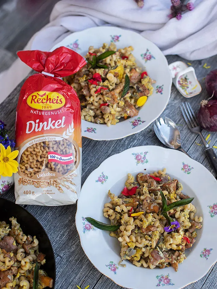 Nudeln mit Ei und Kräutern auf zwei Tellern neben einer Packung Recheis Dinkel Nudeln