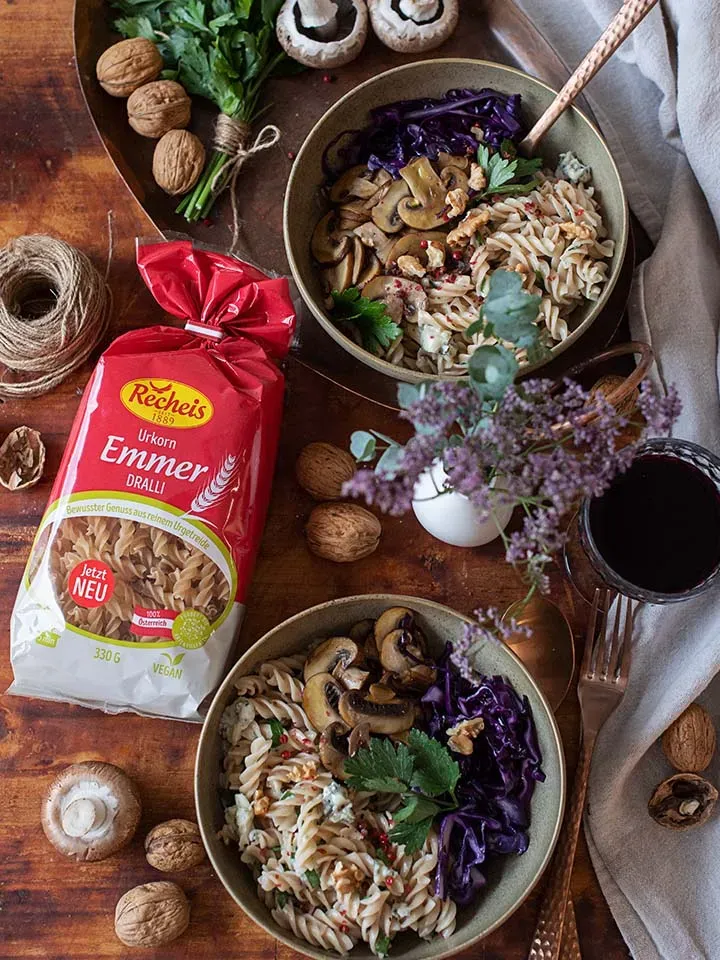 Nudeln mit Gorgonzolasauce, Pilzen, Walnüssen und Rotkohl in zwei Schalen auf Holztisch neben Nudelpackung