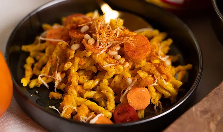 Nudeln mit Karottenpesto, dazu Karottenscheiben und weiße Körner in einer schwarzen Schale