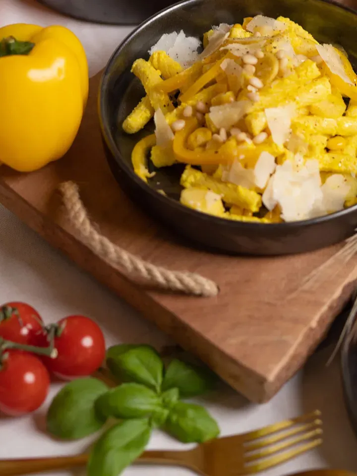 Nudeln mit Paprikacreme: gelbe Pasta mit Parmesan und Pinienkernen in Schüssel auf Holzbrett mit Gemüse