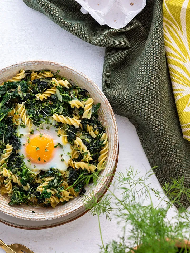 Low-Carb-Nudeln mit Spinat und einem Spiegelei in der Mitte in einer Schüssel auf weißem Tisch