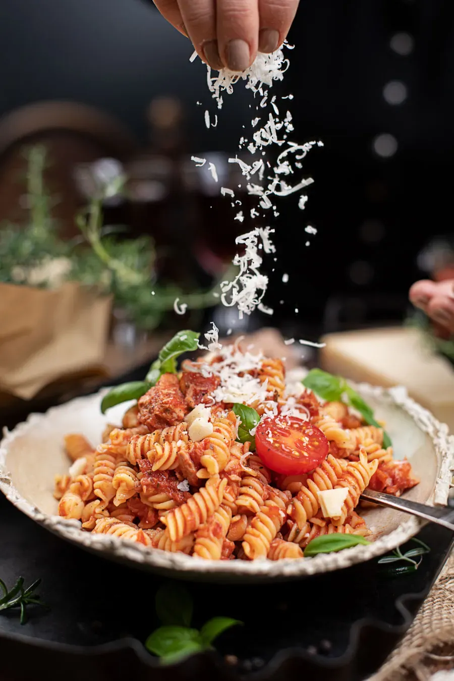 Hand streut geriebenen Käse über Fusilli mit Thunfisch-Tomatensauce, glutenfrei, auf einem Teller