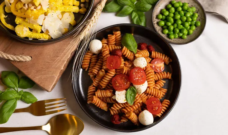 Tomaten-Fusilli mit Tomatensauce, Mozzarella und Basilikum auf einem Teller auf weißem Tisch