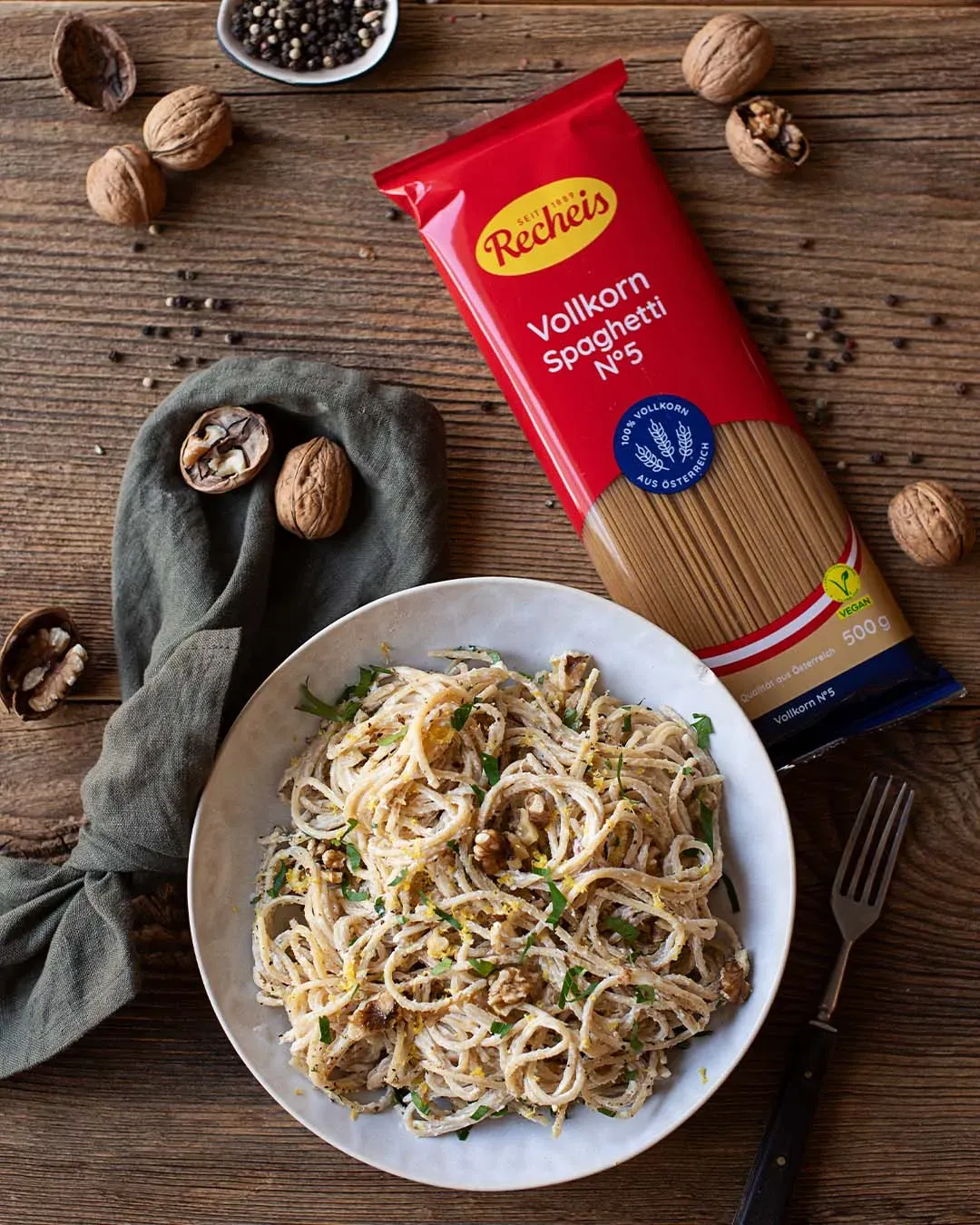 Vollkornspaghetti mit Zitrone und Walnüssen auf weißem Teller neben Packung und Walnüssen