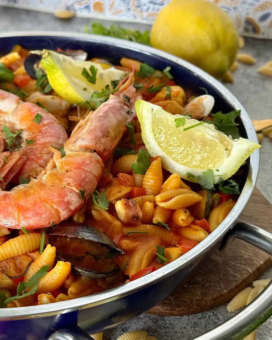 Nudelpaella mit Huhn und Meeresfrüchten in der Pfanne, mit Garnelen, Muscheln und Zitronenscheiben