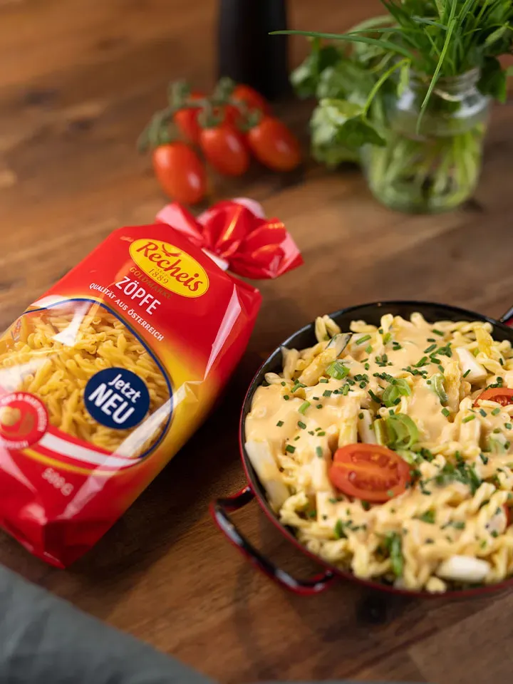 Packung Zöpfe Nudeln neben einem Teller Nudelpfanne mit Spargel, cremiger Sauce und Tomaten