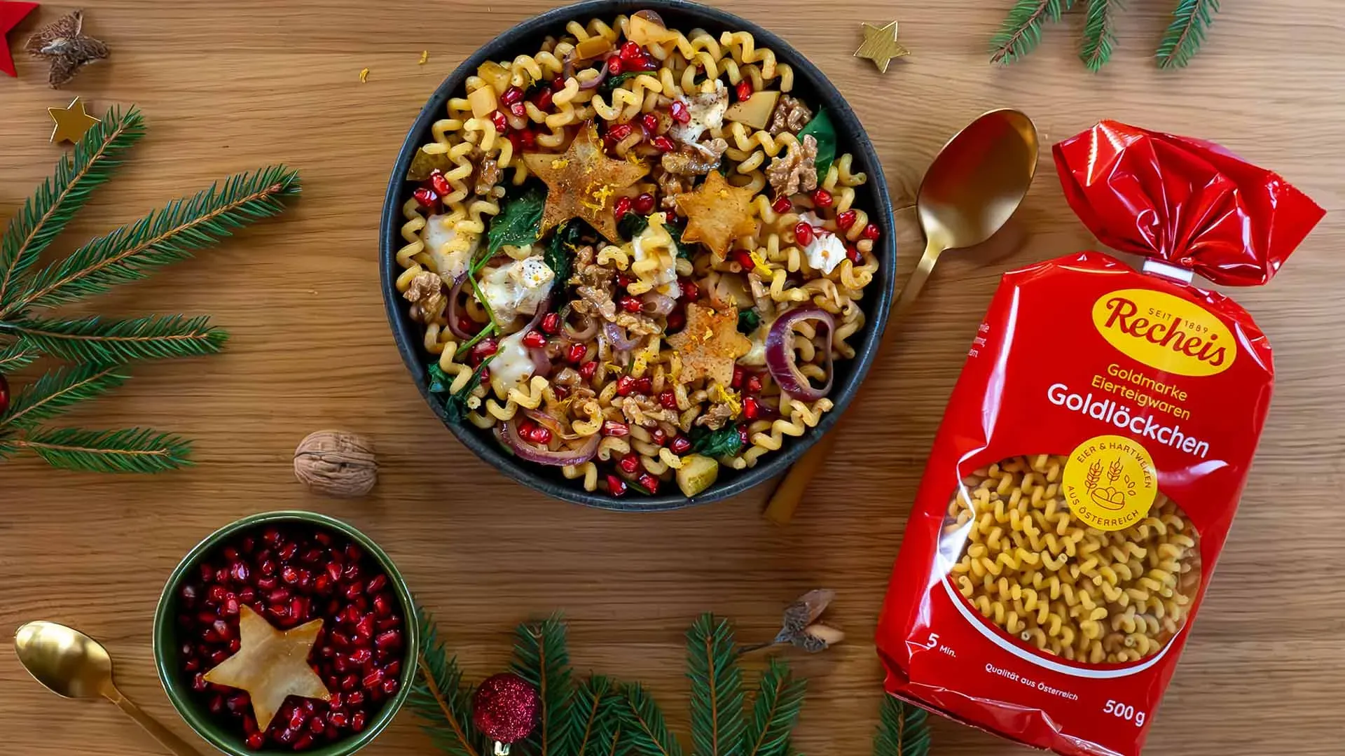 Weihnachtliche Nudelpfanne mit Granatapfelkernen und Sternen aus Teig auf Holzuntergrund