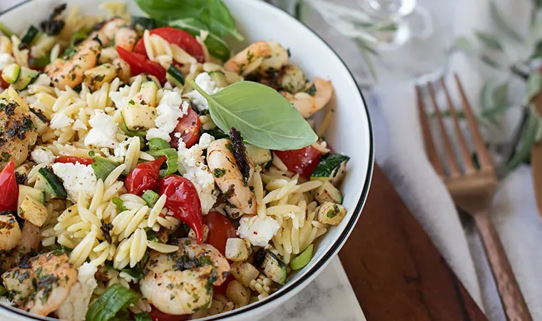 Nudelreis-Salat mit Garnelen, Tomaten, Feta und frischen Kräutern in einer Schüssel