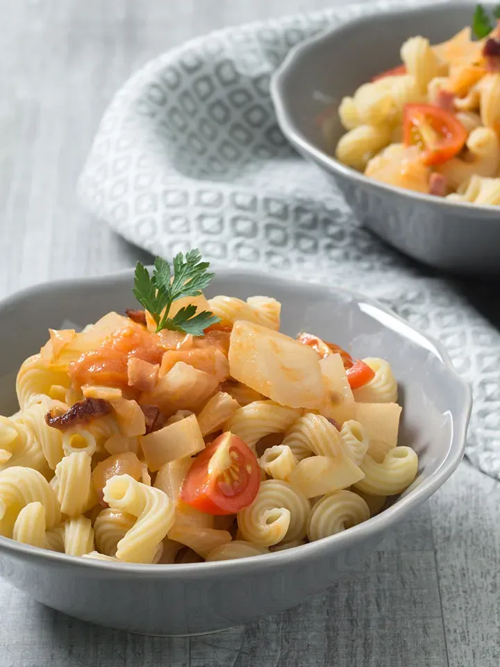 Nudeln mit Fenchel: Schale mit Spiralnudeln, Tomaten und Gemüse auf grauem Tisch