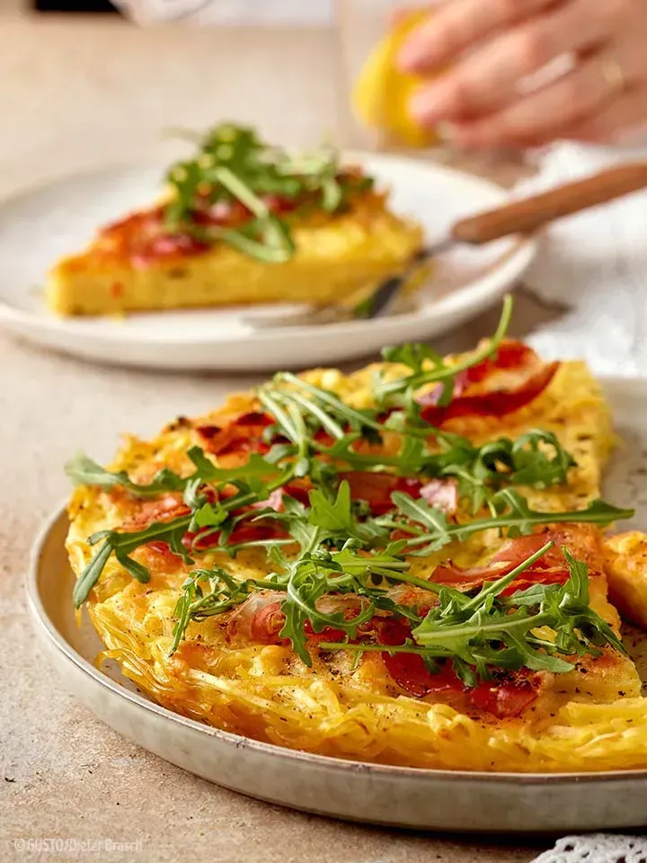 Zwei Stücke Nudelrösti mit Rucola, eines davon auf einem kleinen Teller angerichtet