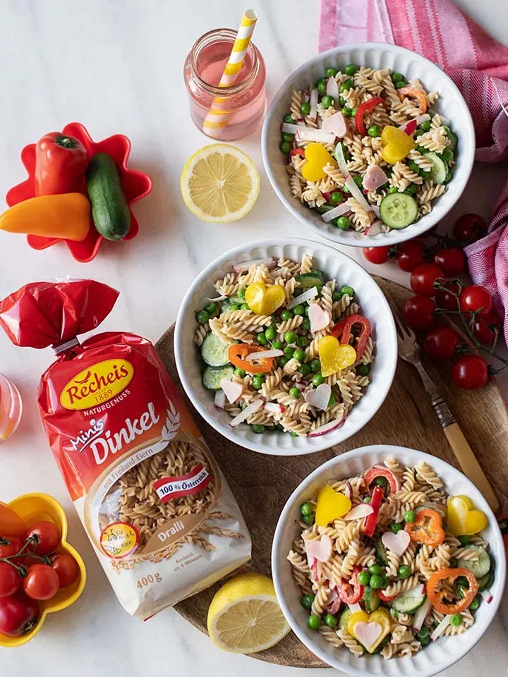Nudelsalat für Kinder mit Dinkelnudeln: drei Schalen mit Gemüse auf einem Tisch mit Pasta und Zitronen