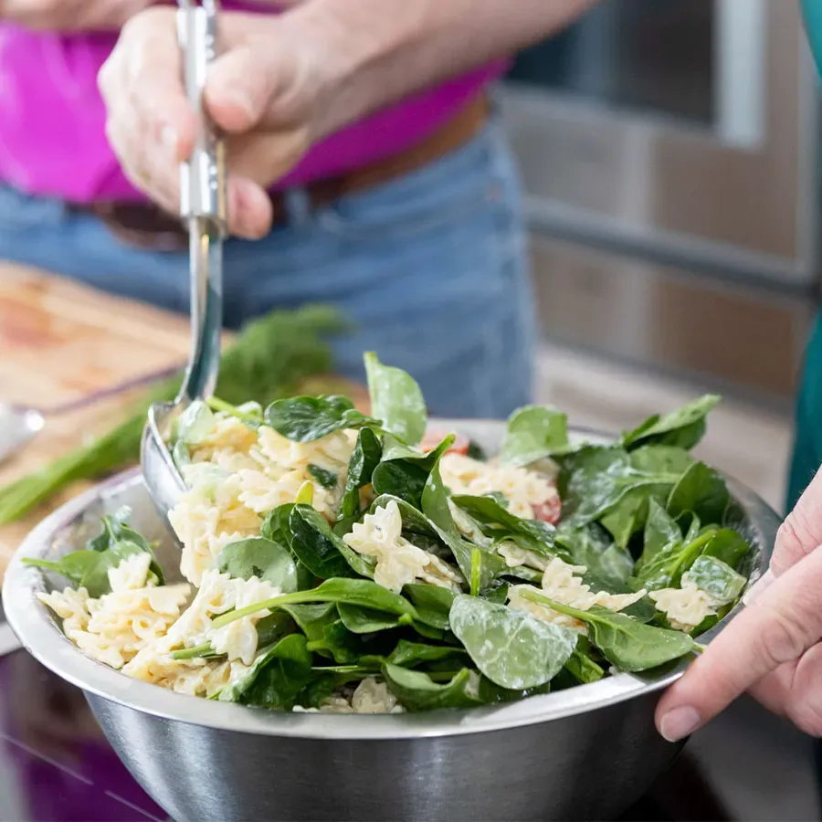 Person rührt Nudelsalat mit Babyspinat in einer Metallschüssel