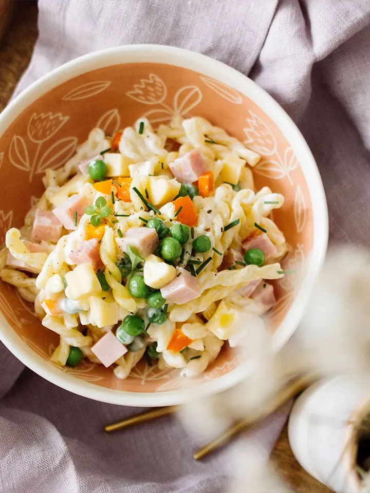 Nudelsalat mit Erbsen aus Spiralnudeln, Schinken und Gemüse in einer Schüssel auf Stoff