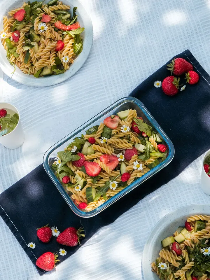 Nudelsalat mit Erdbeeren, Gurken und Blüten auf einem weißen und einem blauen Tuch angerichtet