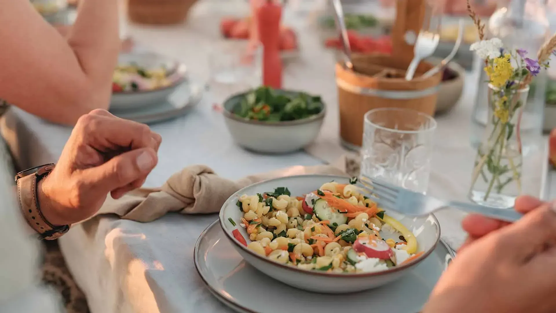 Gedeckter Sommertisch mit einem Teller vegetarischem Nudelsalat mit Feta und Gemüse