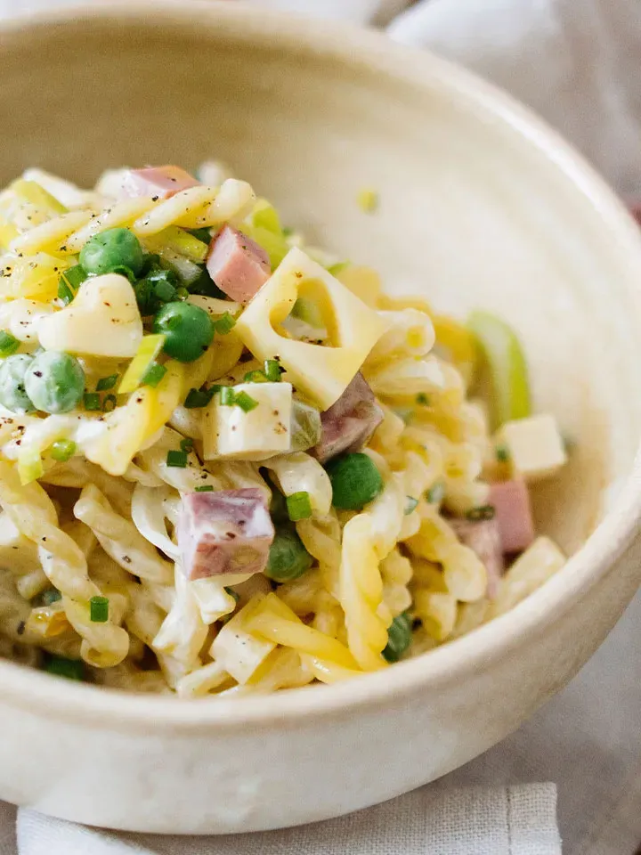 Nudelsalat mit Joghurt, Erbsen, Schinkenwürfeln und Käse in einer Schüssel