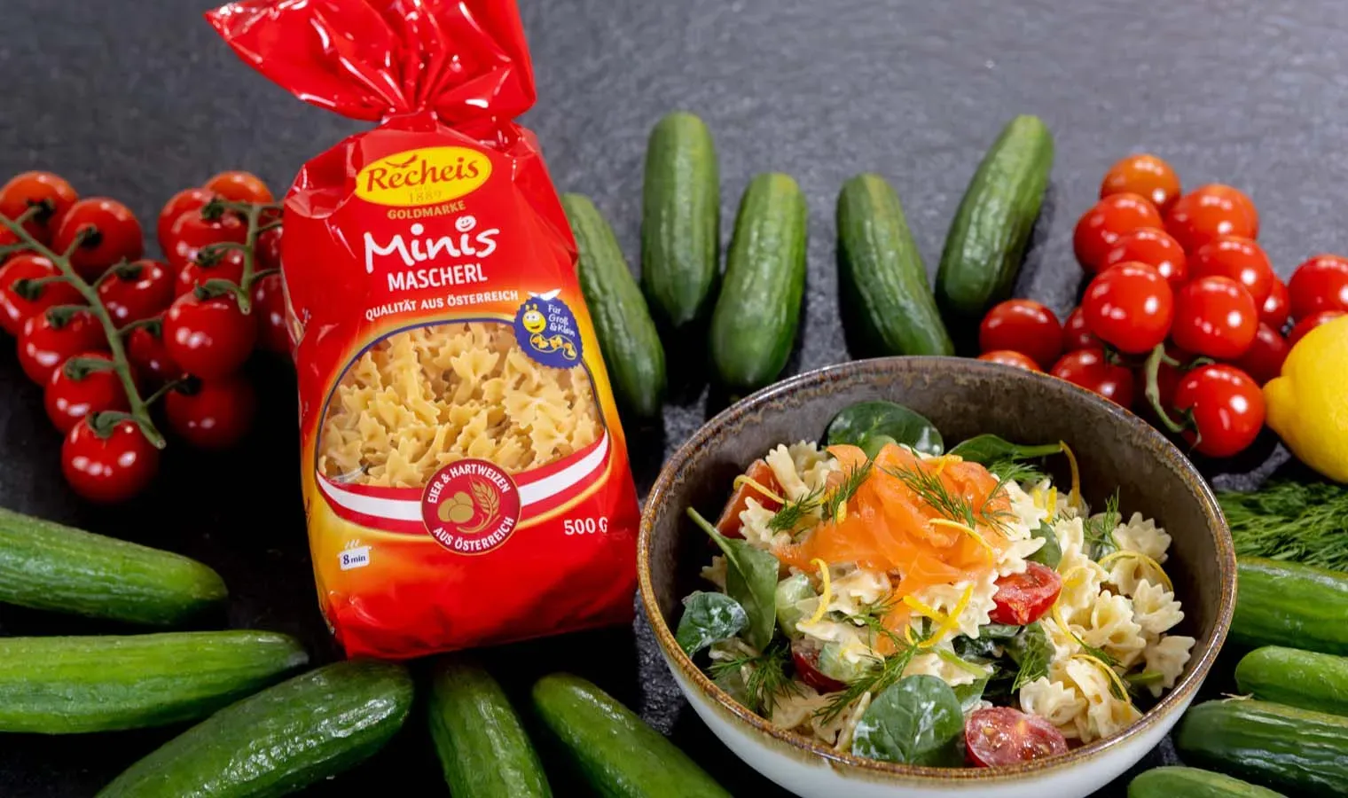 Nudelsalat mit Mascherl, Lachs, Gurken und Tomaten in einer Schüssel neben einer Nudeltüte