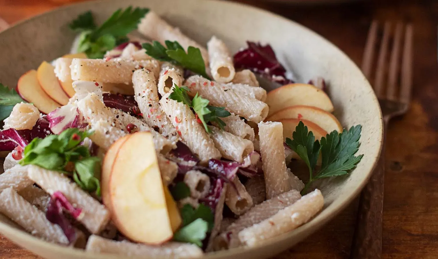 Nudelsalat mit Ricotta, Apfelscheiben, Radicchio und Petersilie auf einem Teller auf Holztisch