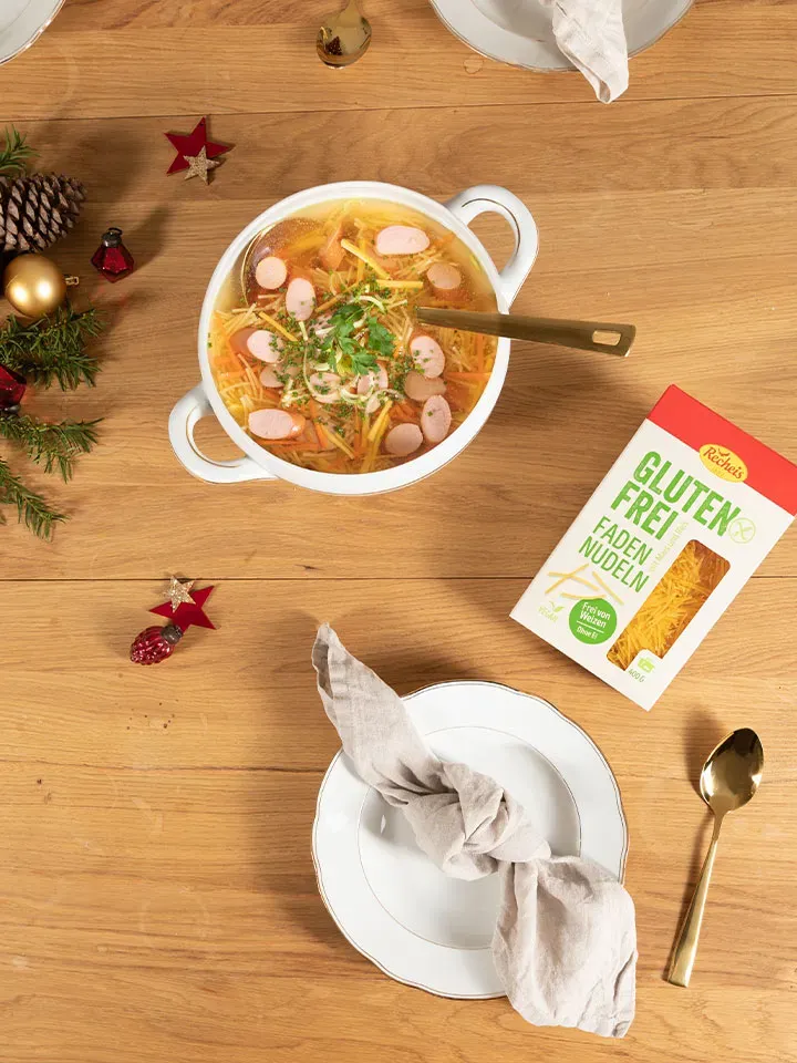 Glutenfreie Nudelsuppe mit Würstchen auf einem Teller mit Serviette auf Holztisch