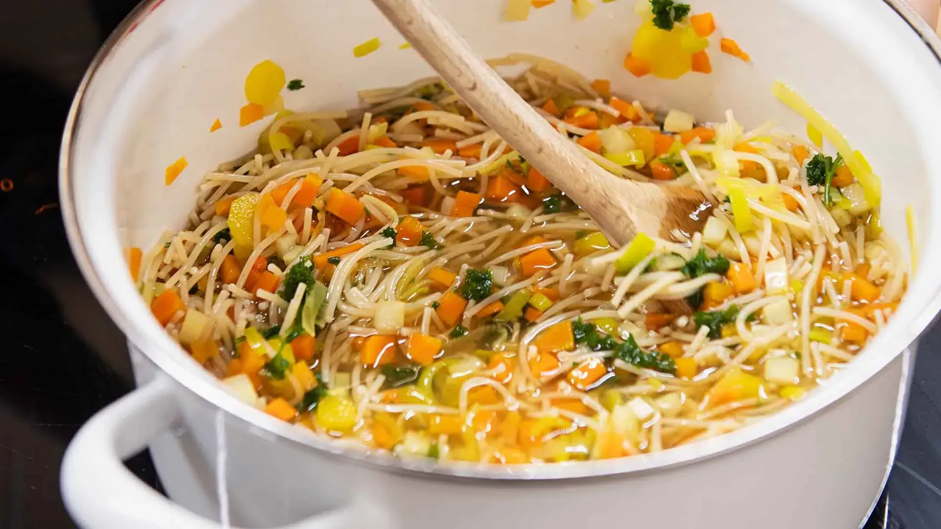 Gemüsesuppe mit Suppennudeln wird im Topf mit einem Holzlöffel umgerührt