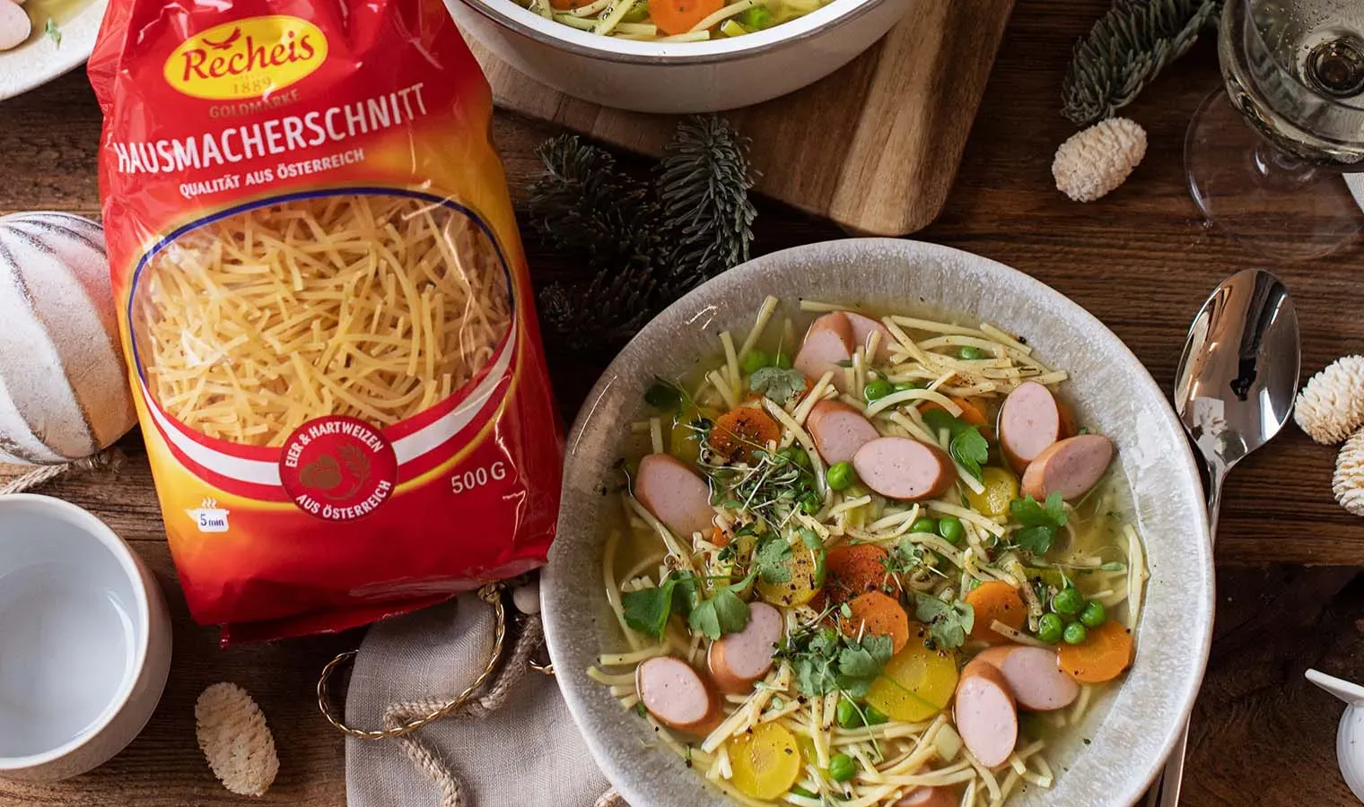 Nudelsuppe mit Würstel auf einem Teller neben einer Packung Recheis Hausmacherschnitt