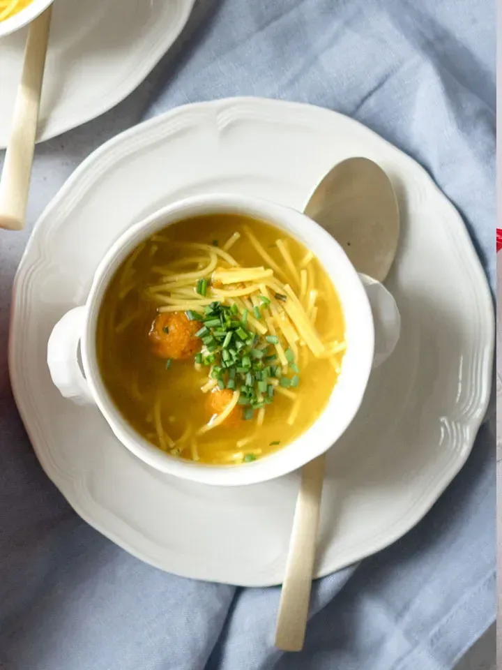 Aufsicht auf eine Suppentasse mit Suppennudeln, Karottenknöderln und frischem Schnittlauch