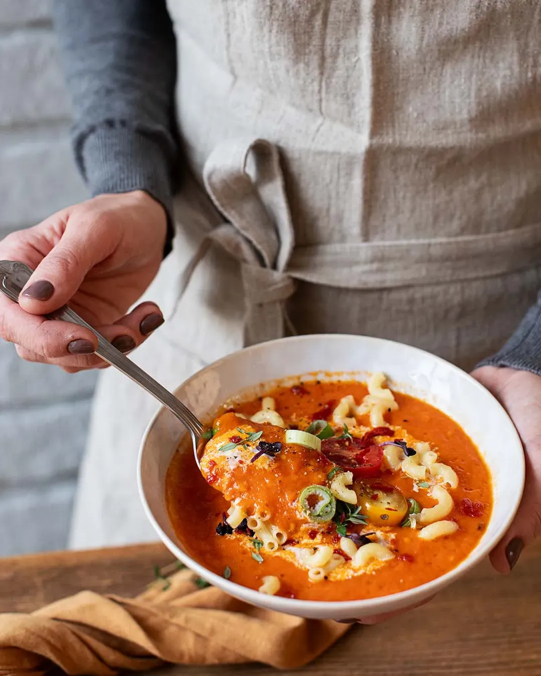 Person hält eine Schüssel mit cremiger Ofentomatensuppe mit Nudeln