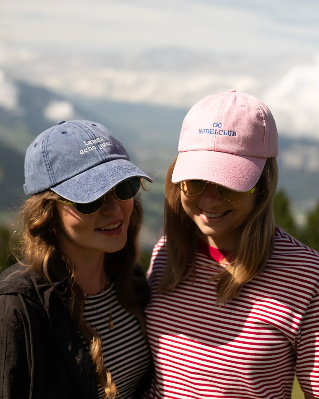 Zwei Frauen mit Baseballcaps und Sonnenbrillen lächeln im Freien