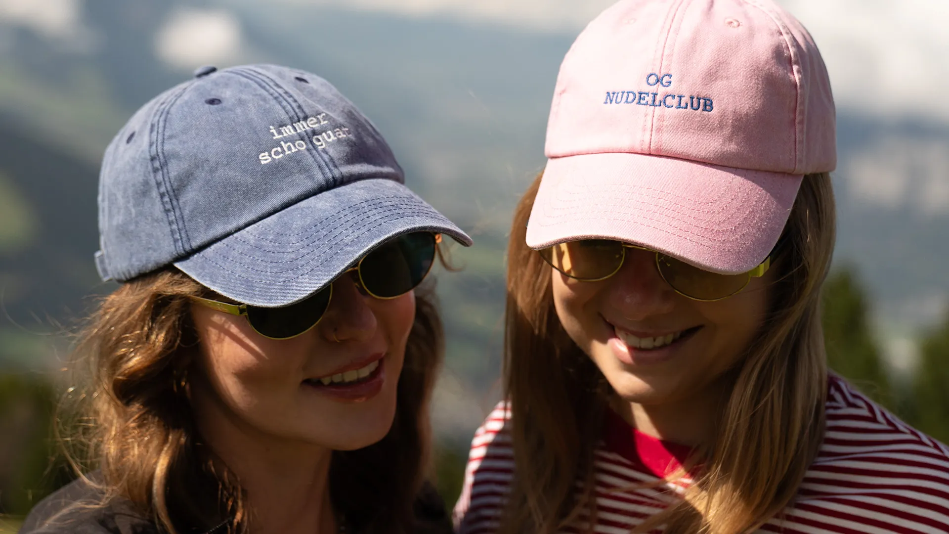 Zwei Frauen mit Sonnenbrillen und Baseballcaps lächeln im Freien