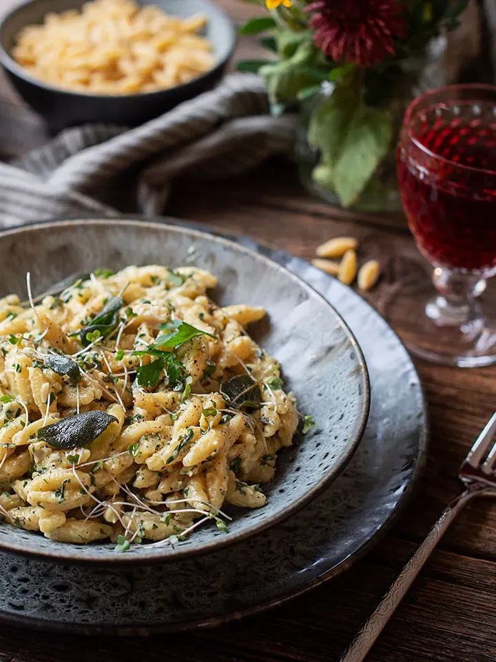One-Pot-Nudelpfanne mit Kräutern auf einem Teller auf Holztisch mit Glas Rotwein und Blumen