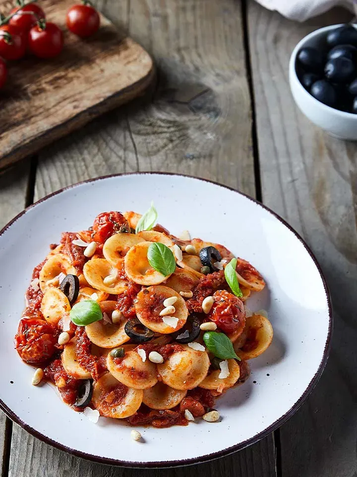 Orecchiette Puttanesca mit Tomatensauce, Oliven und Basilikum auf einem Teller