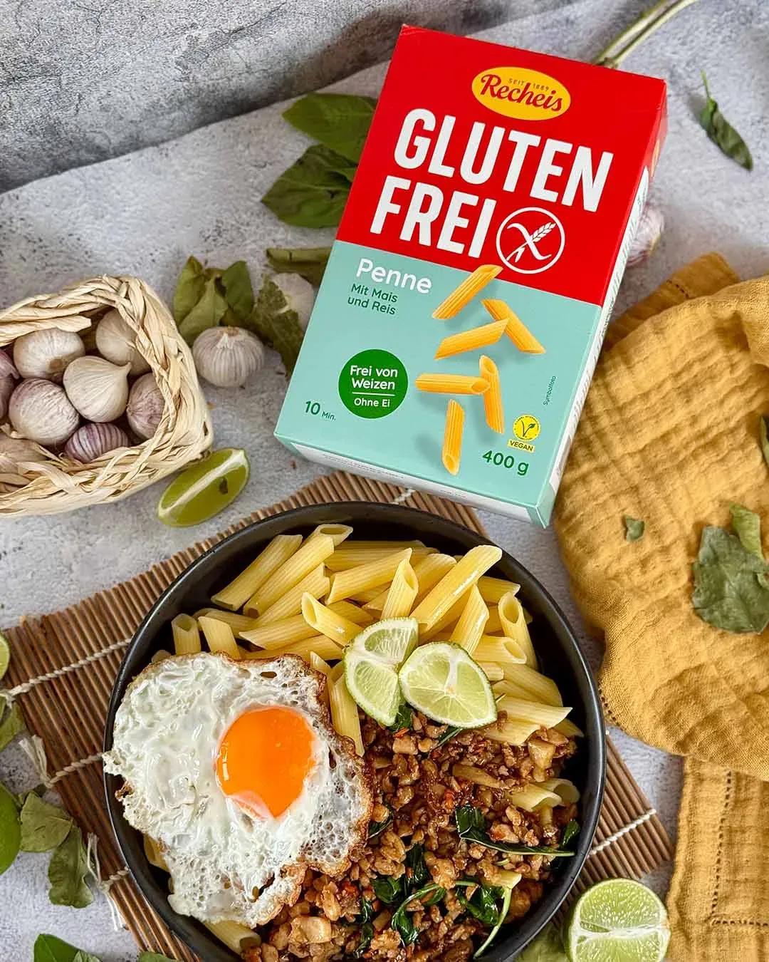 Pad Kra Pao mit glutenfreien Penne, Spiegelei und Hackfleisch in schwarzer Schüssel neben einer Pasta-Packung
