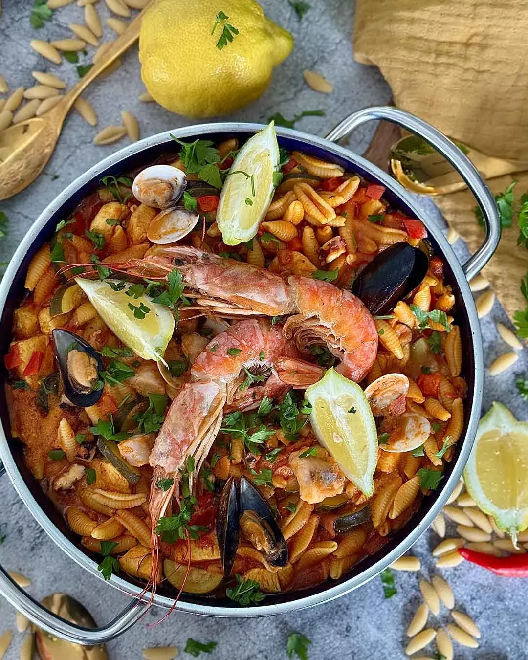 Paella mit Nudeln und Meeresfrüchten im Topf, mit Zitronenscheiben garniert