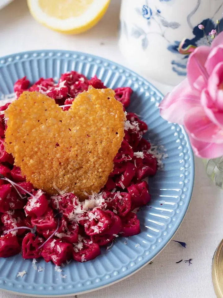 Rote Pasta mit Parmesan und herzförmigem knusprigem Parmesanchip auf einem blauen Teller