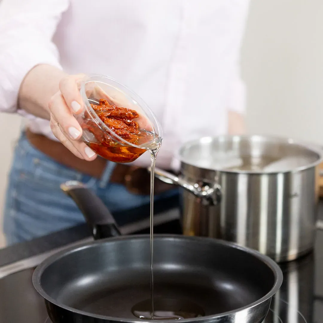 Pasta Arrabbiata mit getrockneten Tomaten: Person gießt Öl mit Tomaten in eine Pfanne