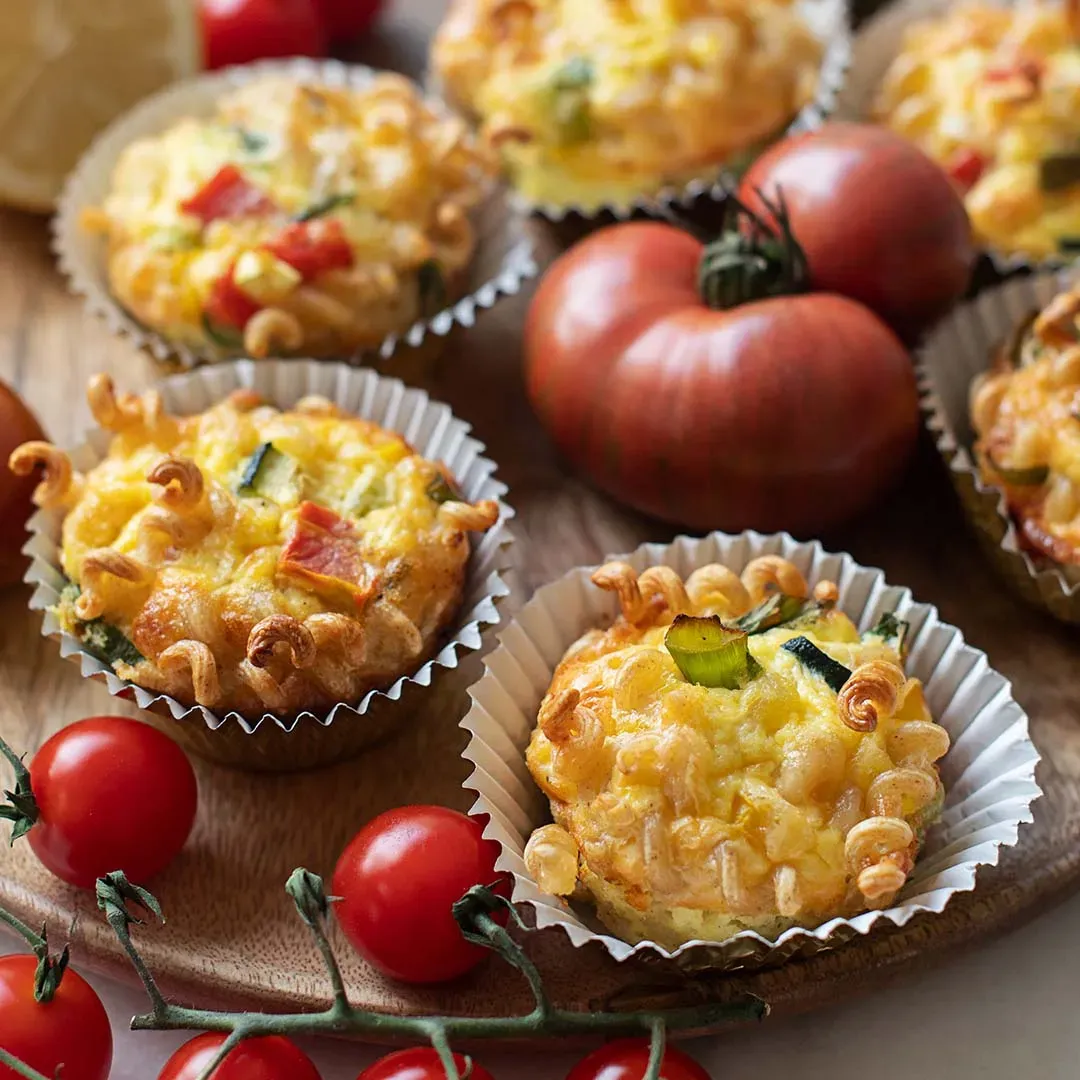 Herzhafte Pasta-Frittata-Muffins mit Gemüse und Tomaten auf einer Holzplatte