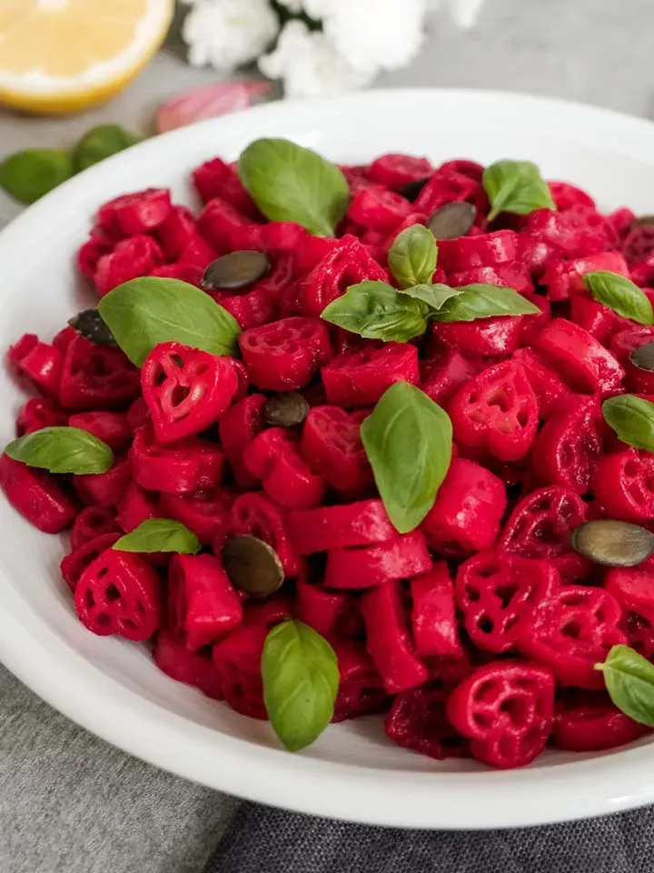 Pasta mit Roter Bete, mit Basilikumblättern und Kürbiskernen auf einem weißen Teller