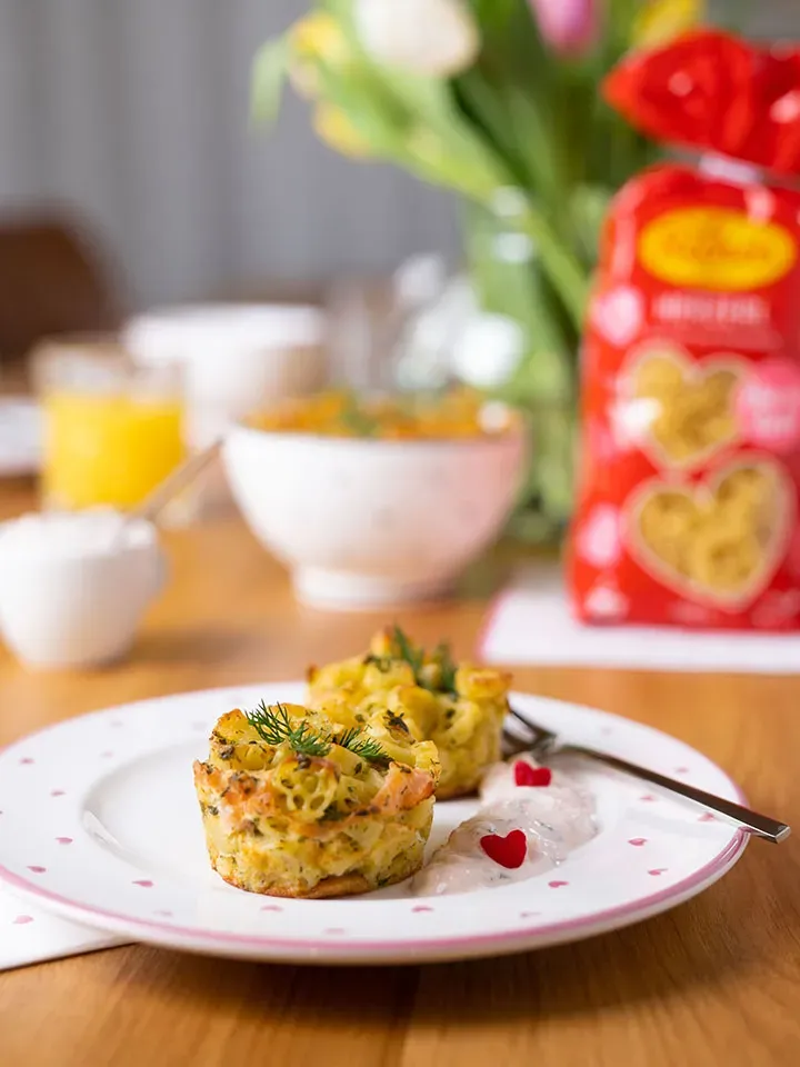 Zwei herzhafte Pastamuffins mit Lachs, Dill und Sauce auf einem Teller mit Herzmuster