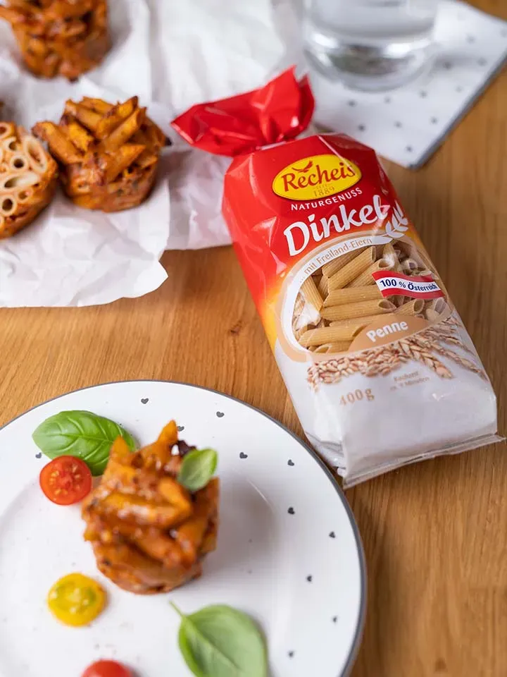 Pastamuffins aus Dinkel-Penne auf einem Teller neben der Packung Dinkel-Penne auf Holztisch