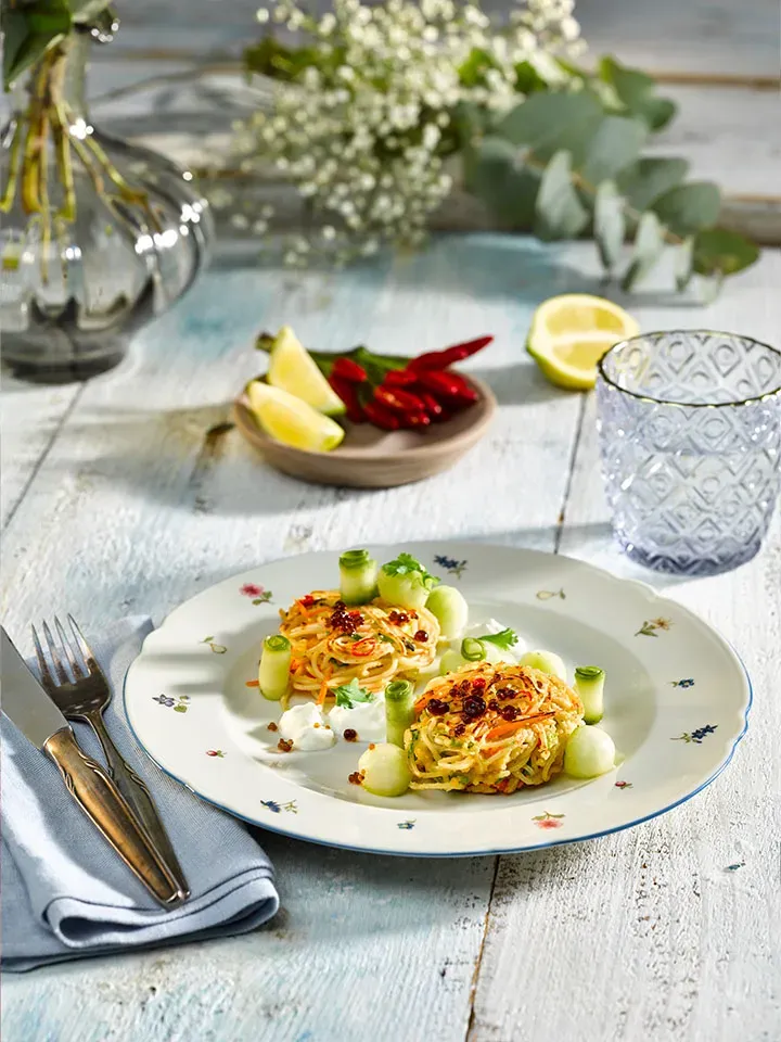 Zwei kleine Pastapuffer aus Spaghetti mit Gemüse, Gurken und Kräutern auf einem Teller