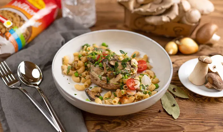 Pilzpfanne mit Tiroler Bio-Pilzen und Pasta, im gefüllten Pilz serviert, mit frischen Kräutern auf Holztisch