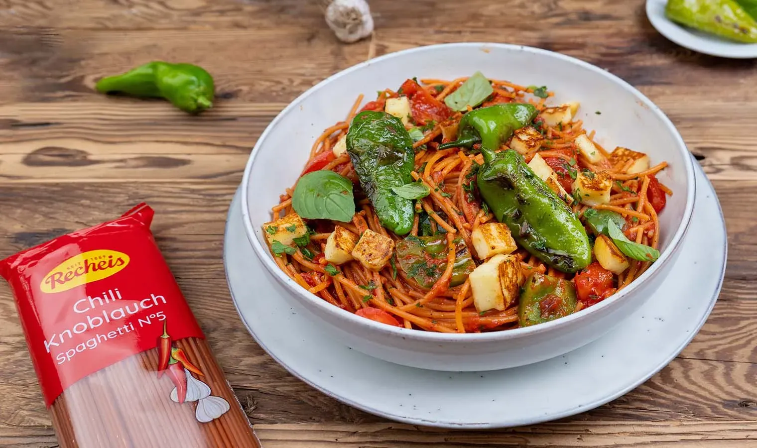 Chili-Knoblauch-Spaghetti mit Pimientos de Padrón und grünen Paprikaschoten auf einem Teller auf Holztisch
