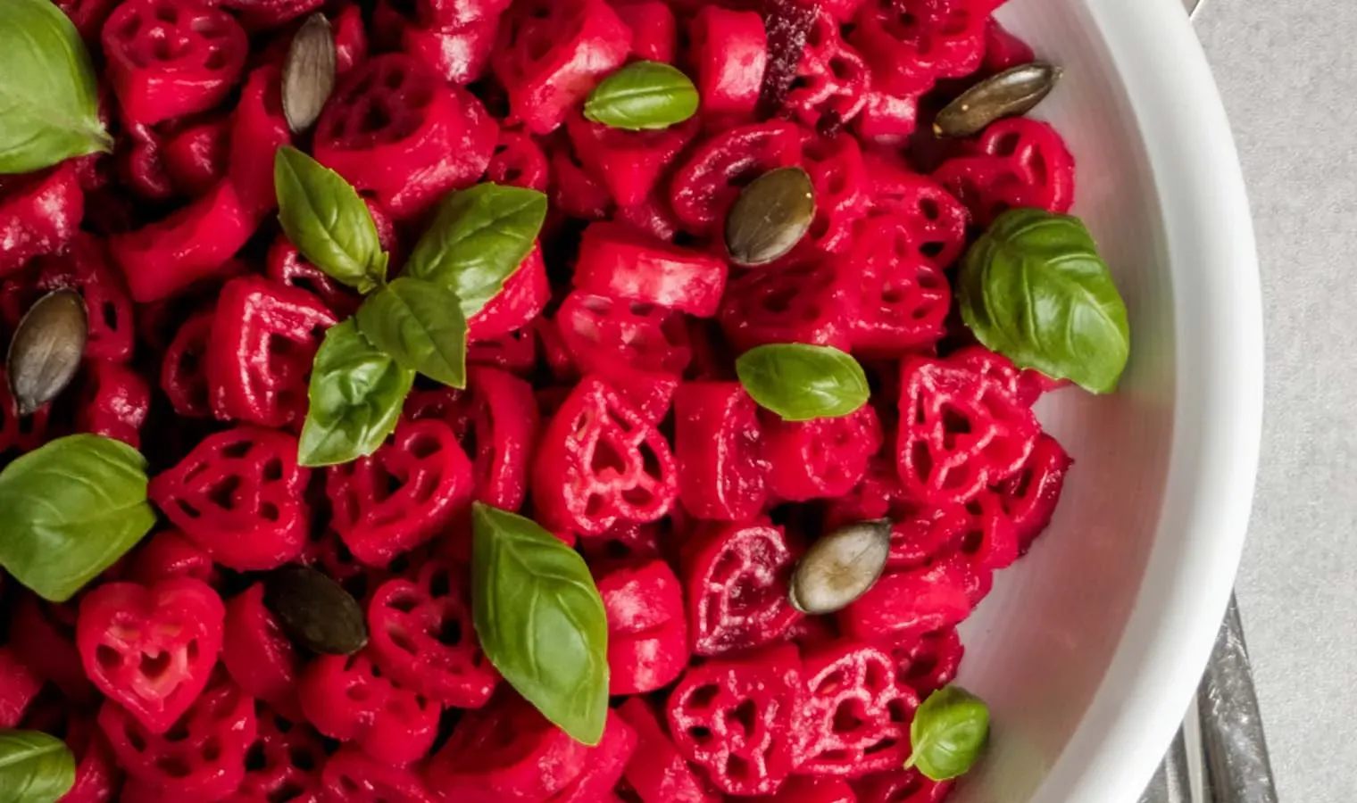 Rote Herznudeln in pinker Rote-Rüben-Sauce mit Basilikumblättern und Kürbiskernen in einer weißen Schüssel