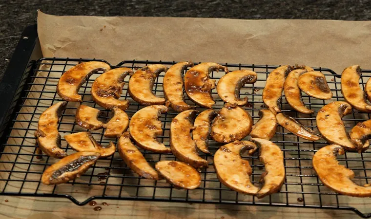 Portobello-Bacon marinieren: gegrillte Pilzscheiben auf einem Gitterrost über Backpapier